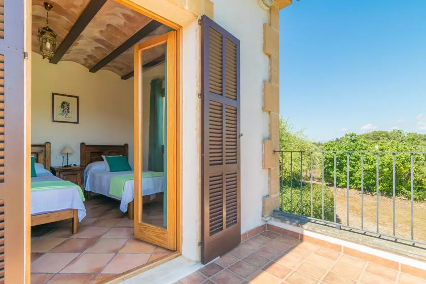 Un dormitorio da a un balcón embaldosado con barandilla metálica y vistas verdes.