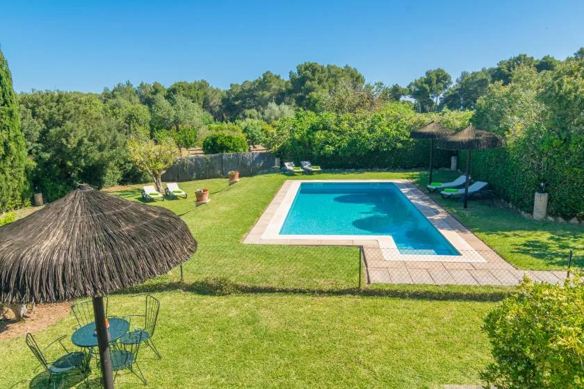Una piscina al aire libre está en un jardín con césped y rodeado de árboles.
