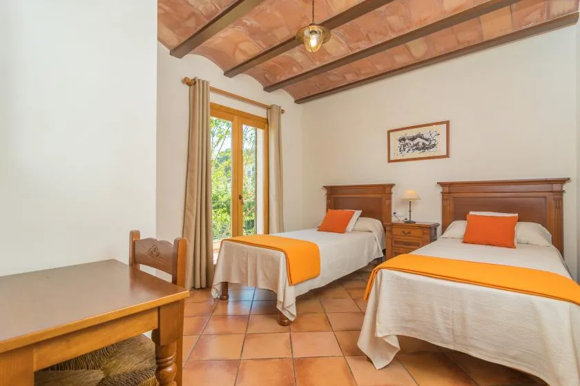 Un dormitorio con dos camas, caminos de cama naranjas y vigas expuestas en el techo.