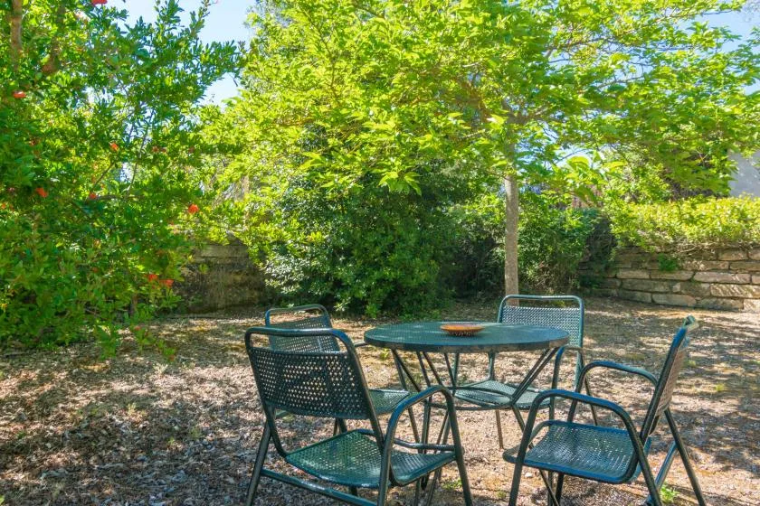 Una zona de estar en el jardín con una mesa redonda bajo árboles frondosos.