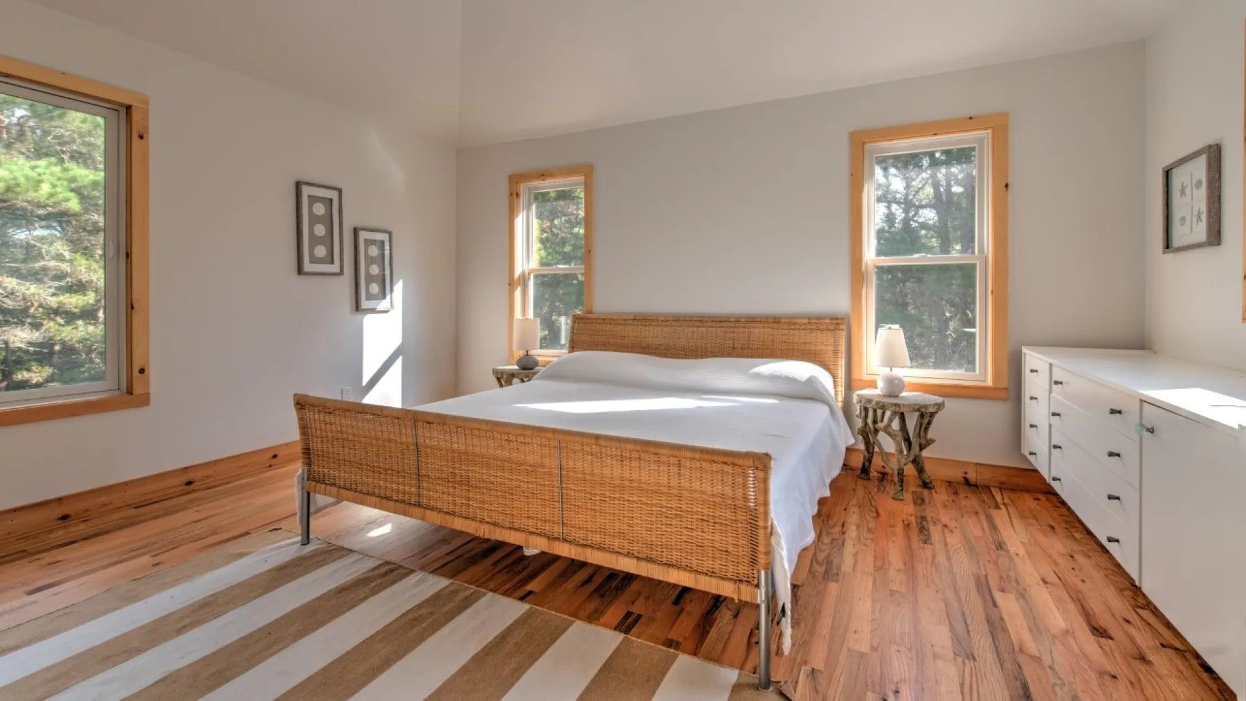 Dormitorio con una cama de tejido, ropa de cama blanca y suelo de madera.