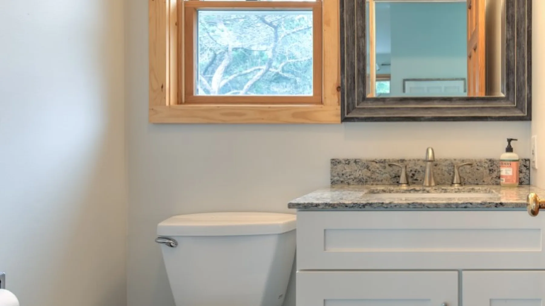 Un baño con lavabo, espejo e inodoro bajo una ventana.
