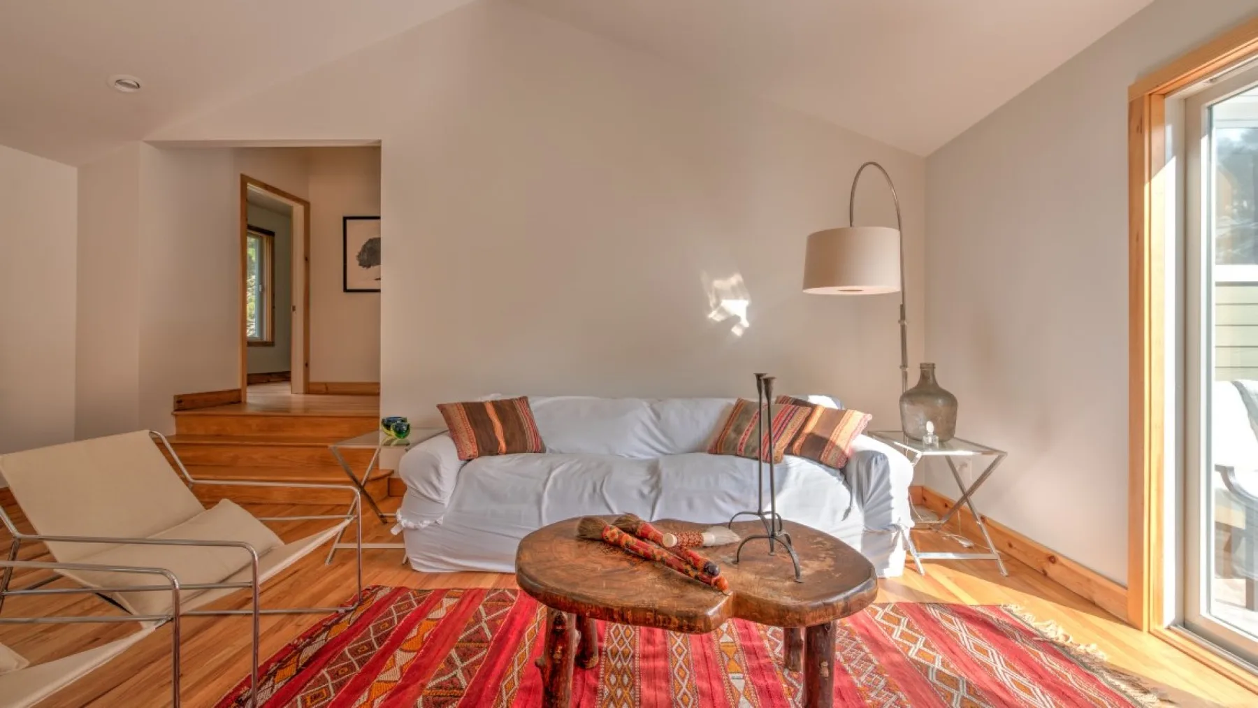 Una sala luminosa con asientos, una mesa de centro de madera y una alfombra colorida.