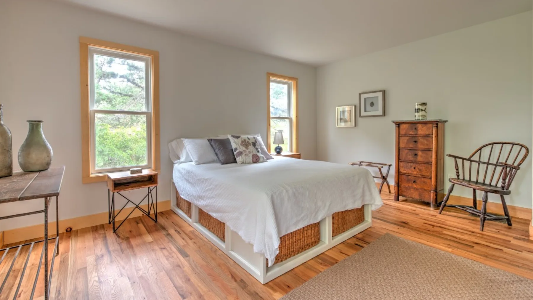 Un dormitorio con una cama tendida, suelo de madera y dos ventanas.