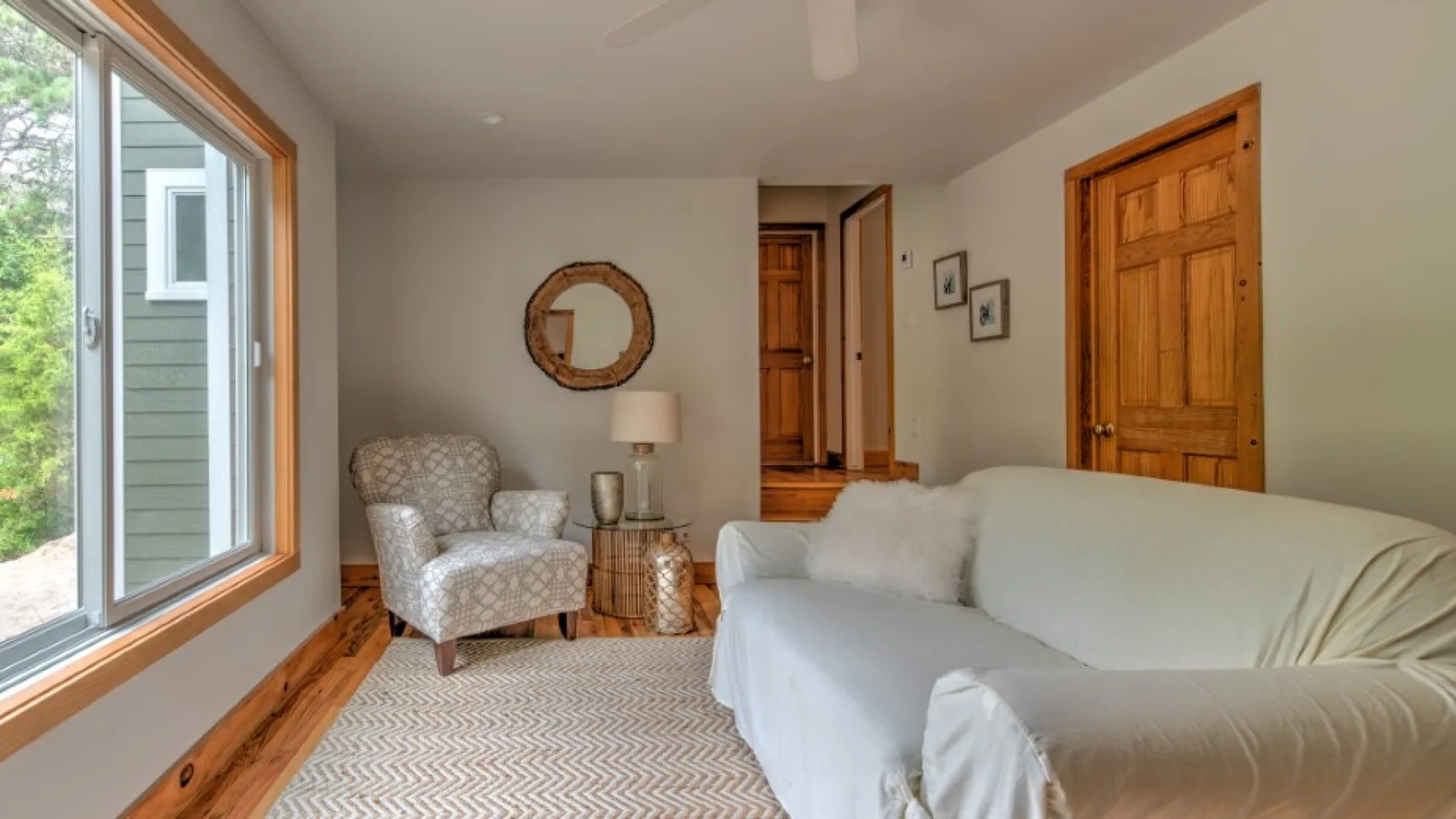 Una sala de estar luminosa con un sofá claro, un sillón y una ventana amplia.