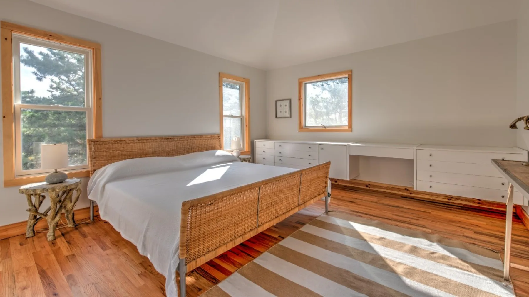Un dormitorio luminoso con una cama, suelo de madera y ventanas.