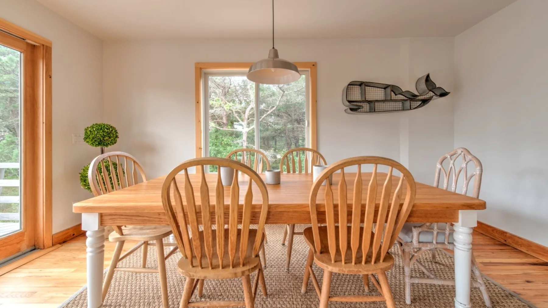 Un comedor luminoso con una mesa y sillas de madera junto a grandes ventanas.