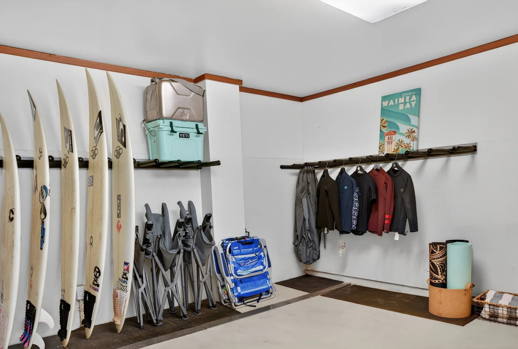Un cuarto de almacenamiento de tablas de surf, con tablas, sillas plegables y chaquetas colgadas.