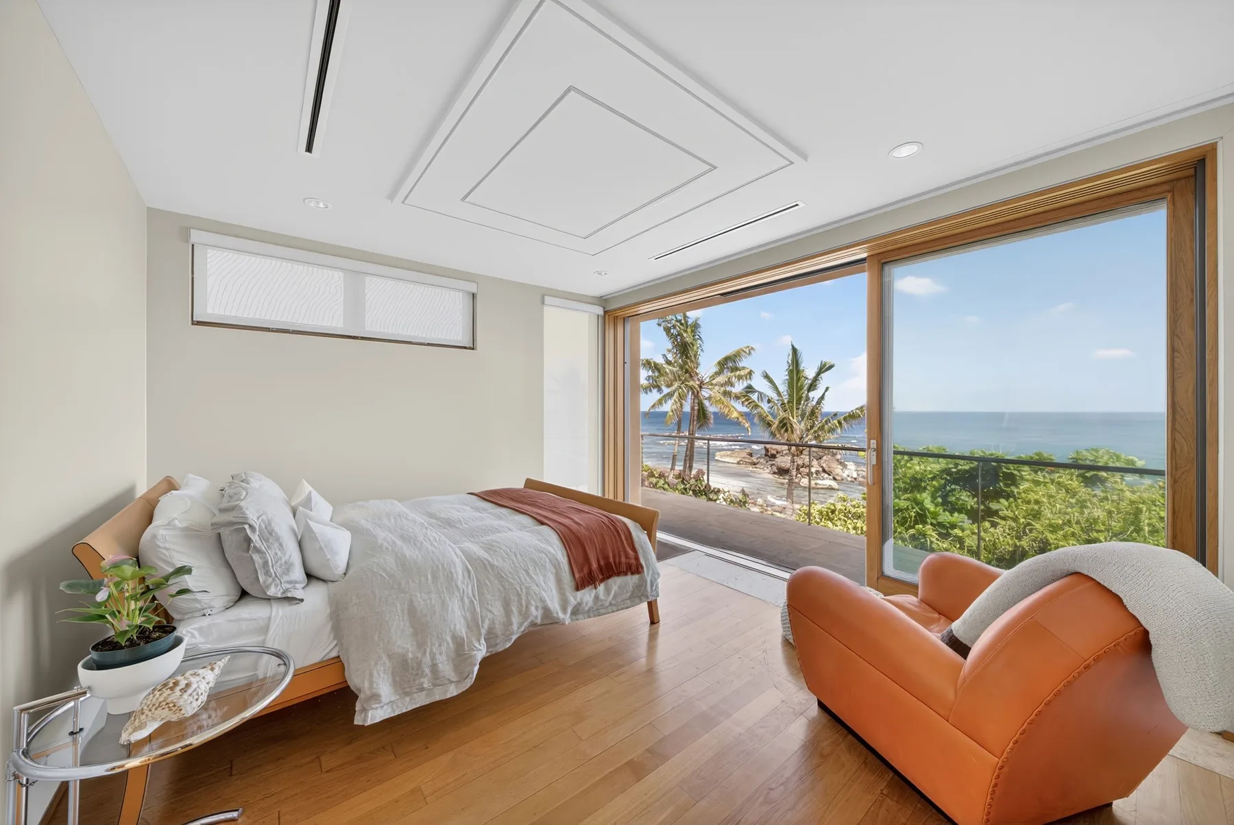 Un dormitorio luminoso con una cama y asientos junto a grandes ventanales con vistas al mar.