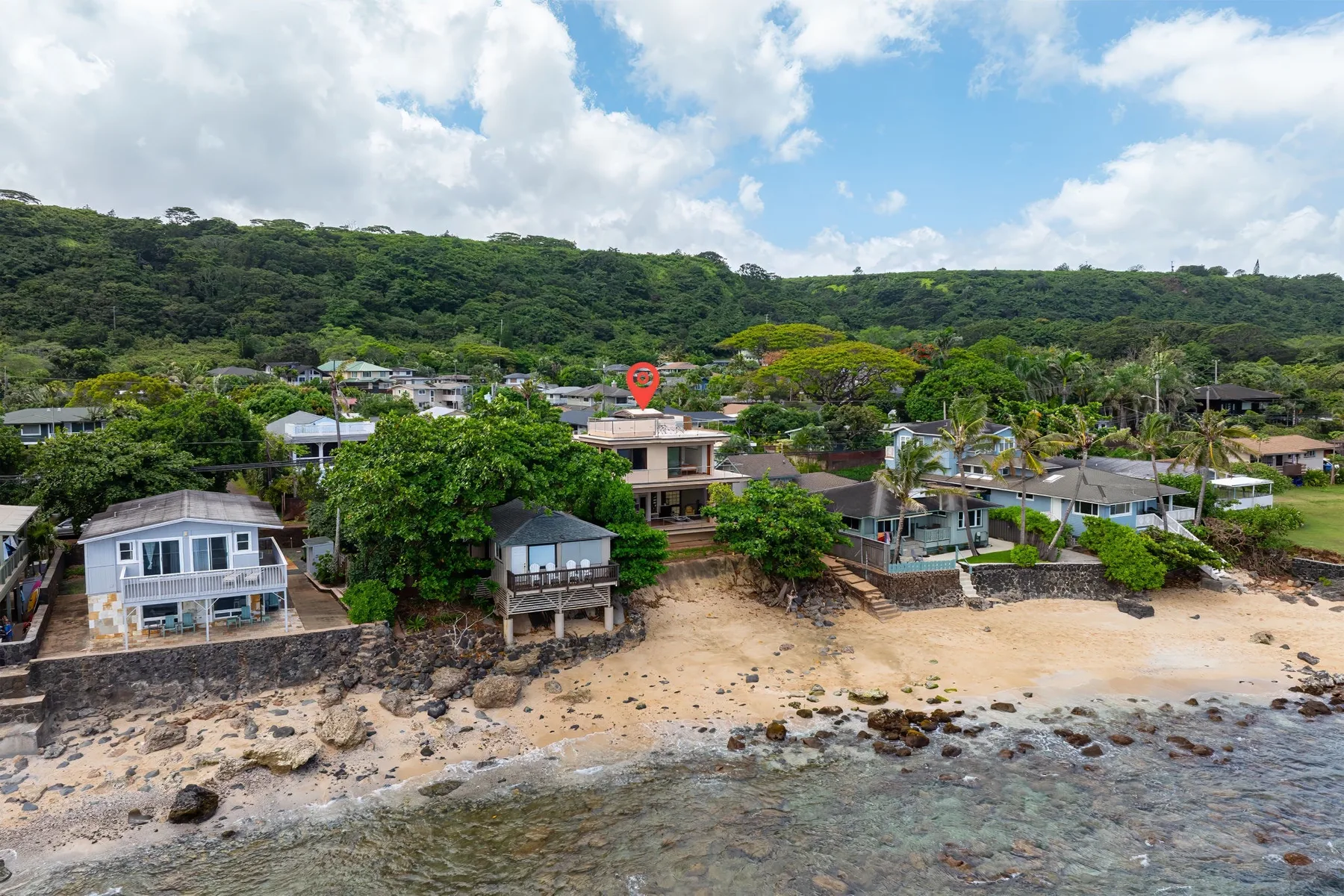 Un barrio costero con casas se extiende junto a una playa de arena bajo una colina verde.