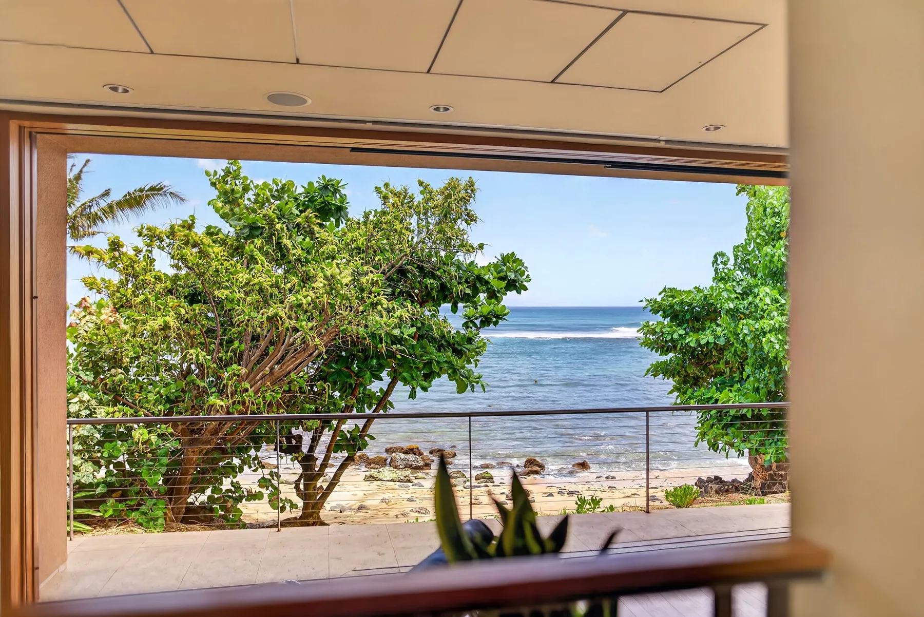 Una ventana amplia enmarca árboles frondosos y una vista del océano.