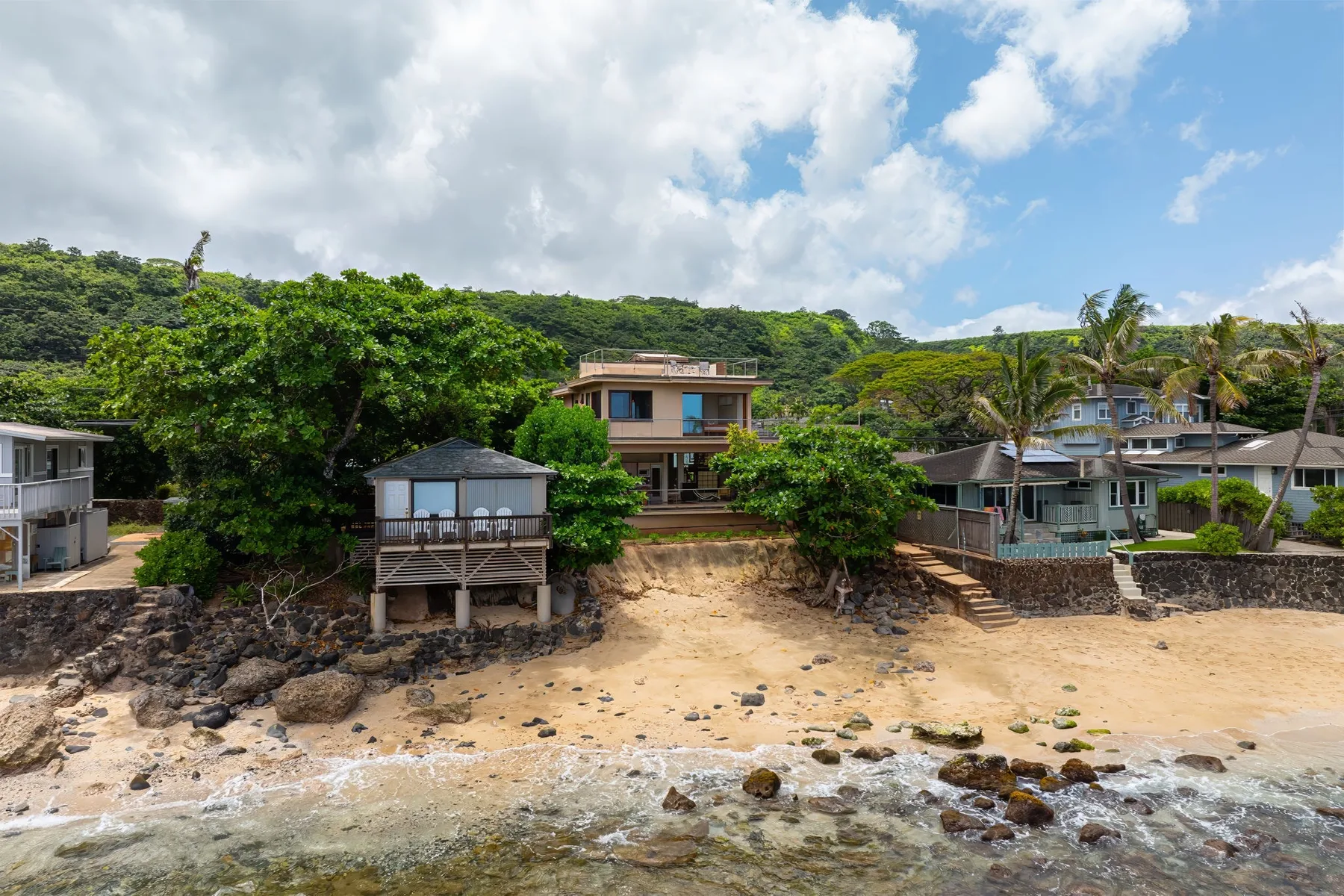 Una escena frente al mar con casas, árboles y una orilla de arena.