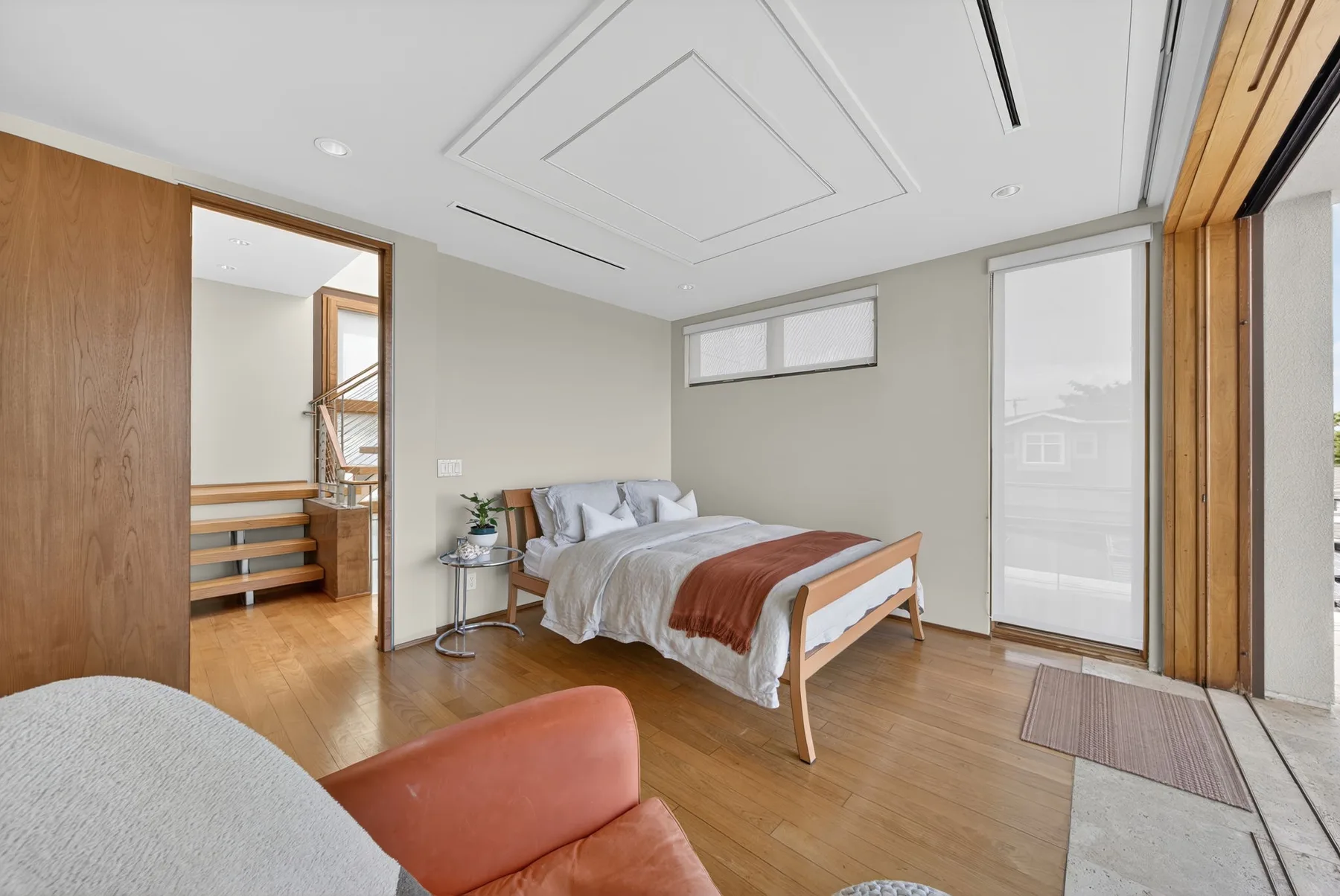 Un dormitorio luminoso con una cama, suelo de madera y ventanales.