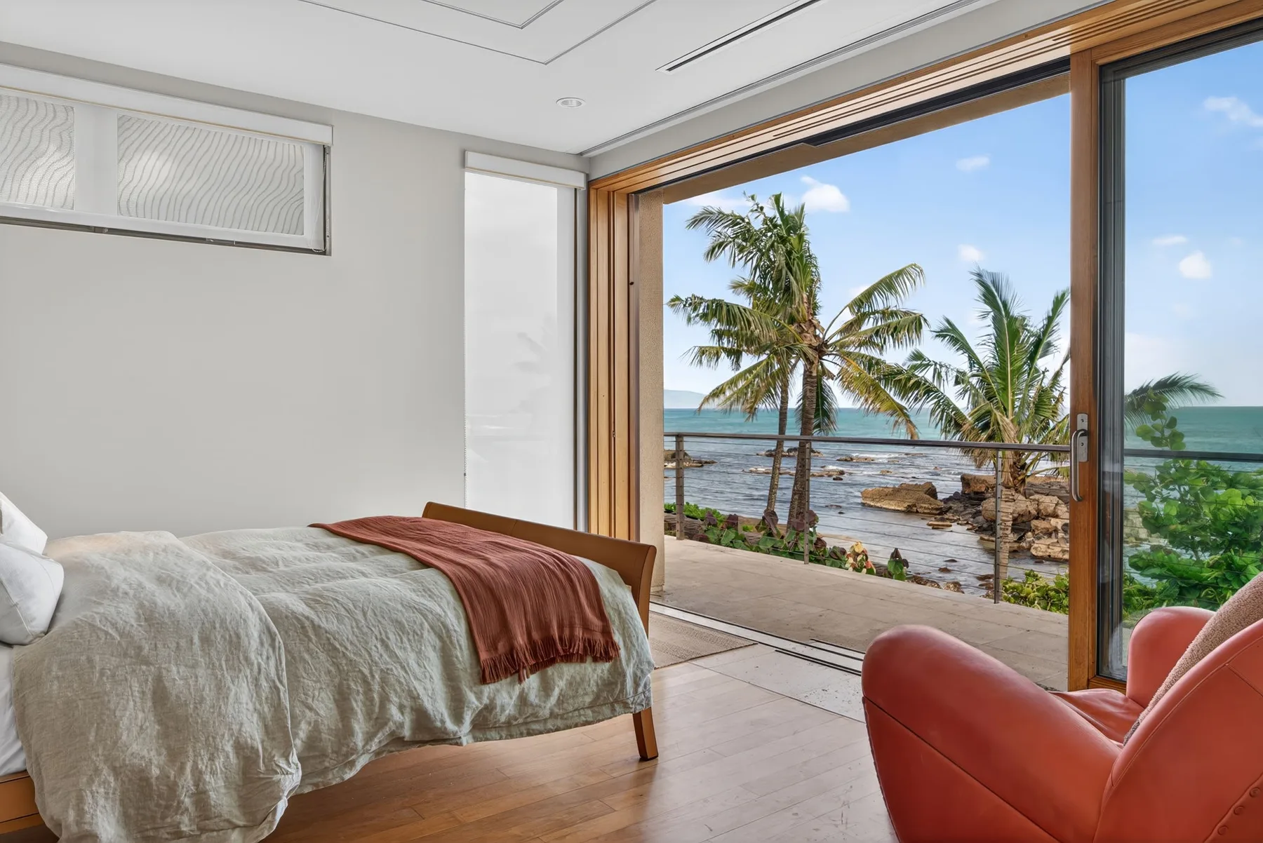 Un dormitorio se abre a un balcón con palmeras y vista al mar.