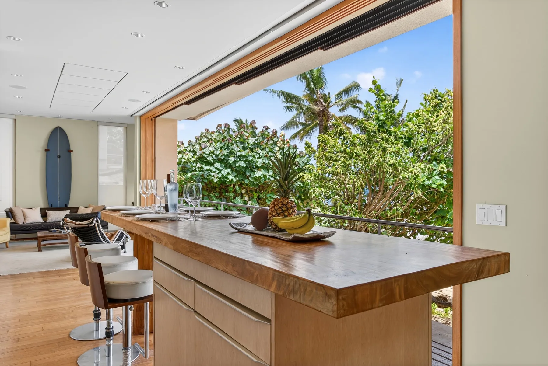 Una barra de cocina y asientos dan a una frondosa vegetación tropical a través de una amplia ventana abierta.