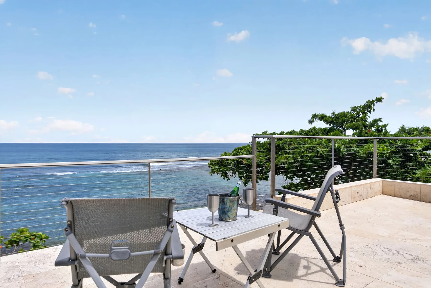 Una terraza junto al mar tiene una mesa pequeña y asientos con vista al océano.