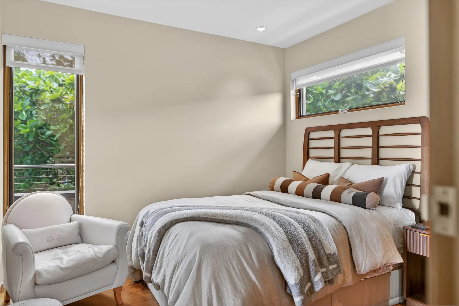 Un dormitorio con una cama, un sillón y ventanas con vistas a la vegetación.