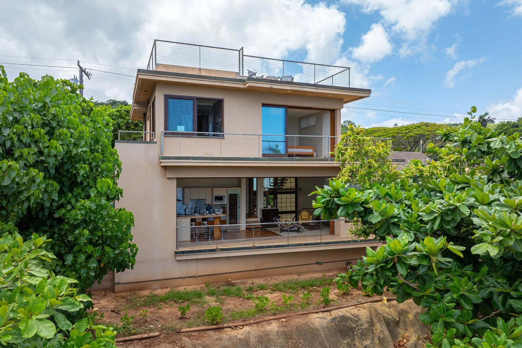 Una casa moderna de dos plantas con balcones está rodeada de vegetación frondosa.
