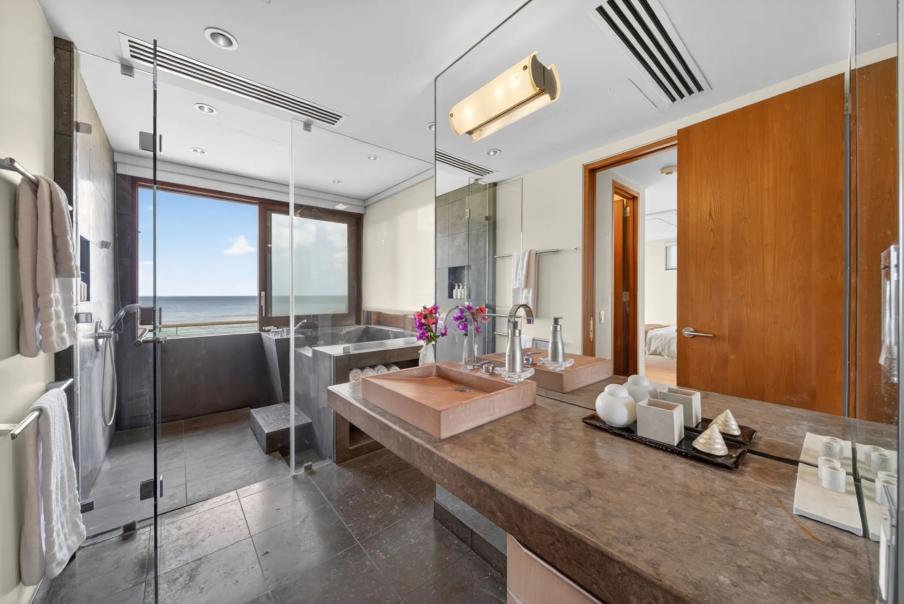 Un baño amplio con lavabo de piedra, ducha de cristal y grandes ventanas con vistas al mar.