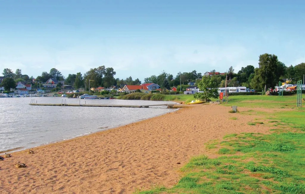 A sandy beach borders calm water, with trees and buildings along the shore.