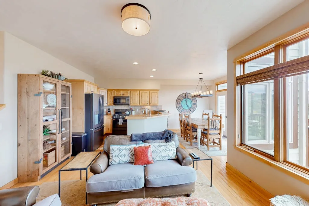 A bright living room opens into a kitchen and dining area, with large windows.