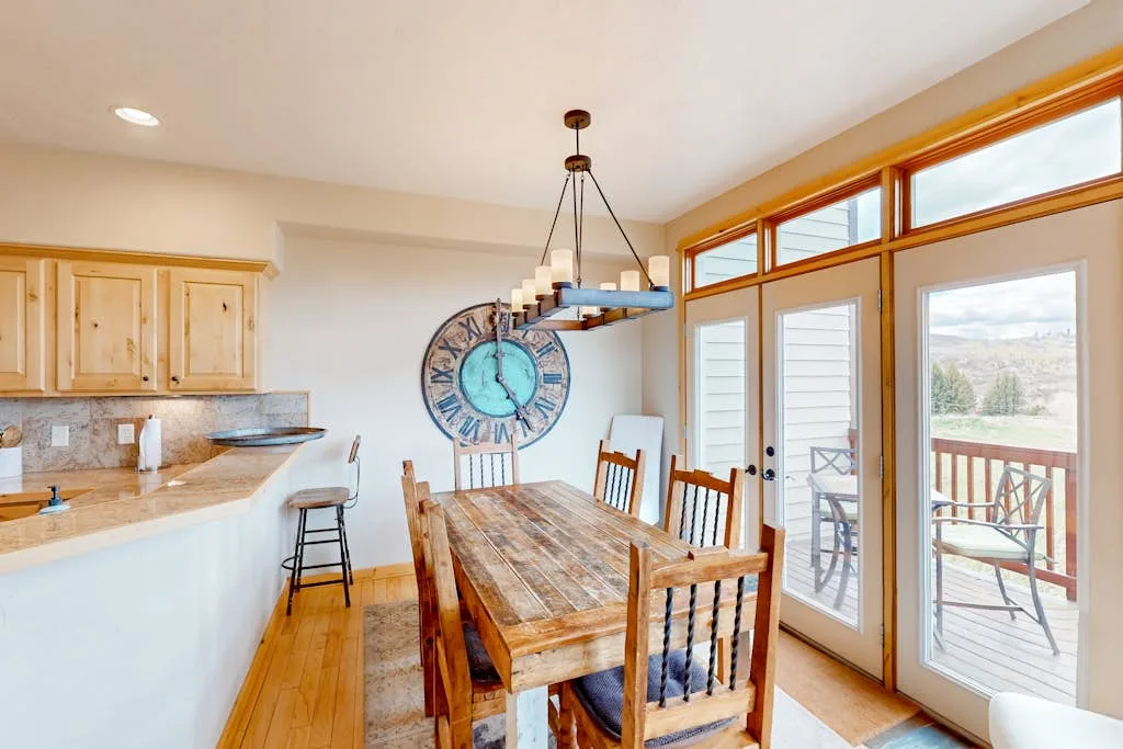 Un comedor luminoso tiene una mesa de madera junto a una barra de cocina y puertas de vidrio.
