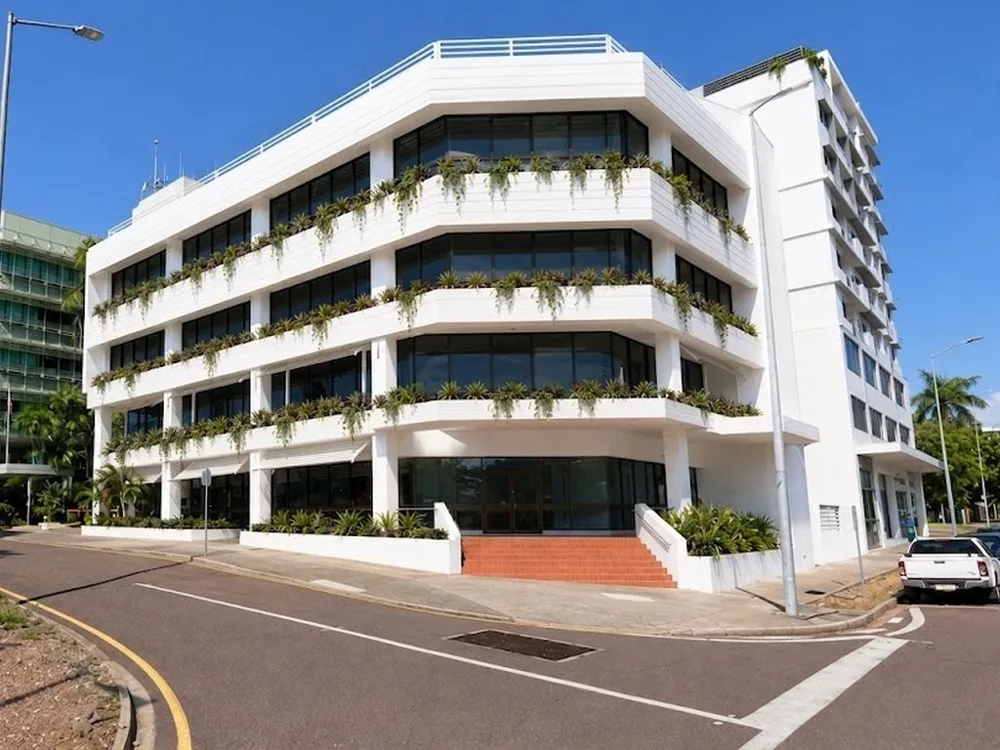 Un edificio blanco moderno con ventanas de vidrio y balcones con plantas está junto a una calle.