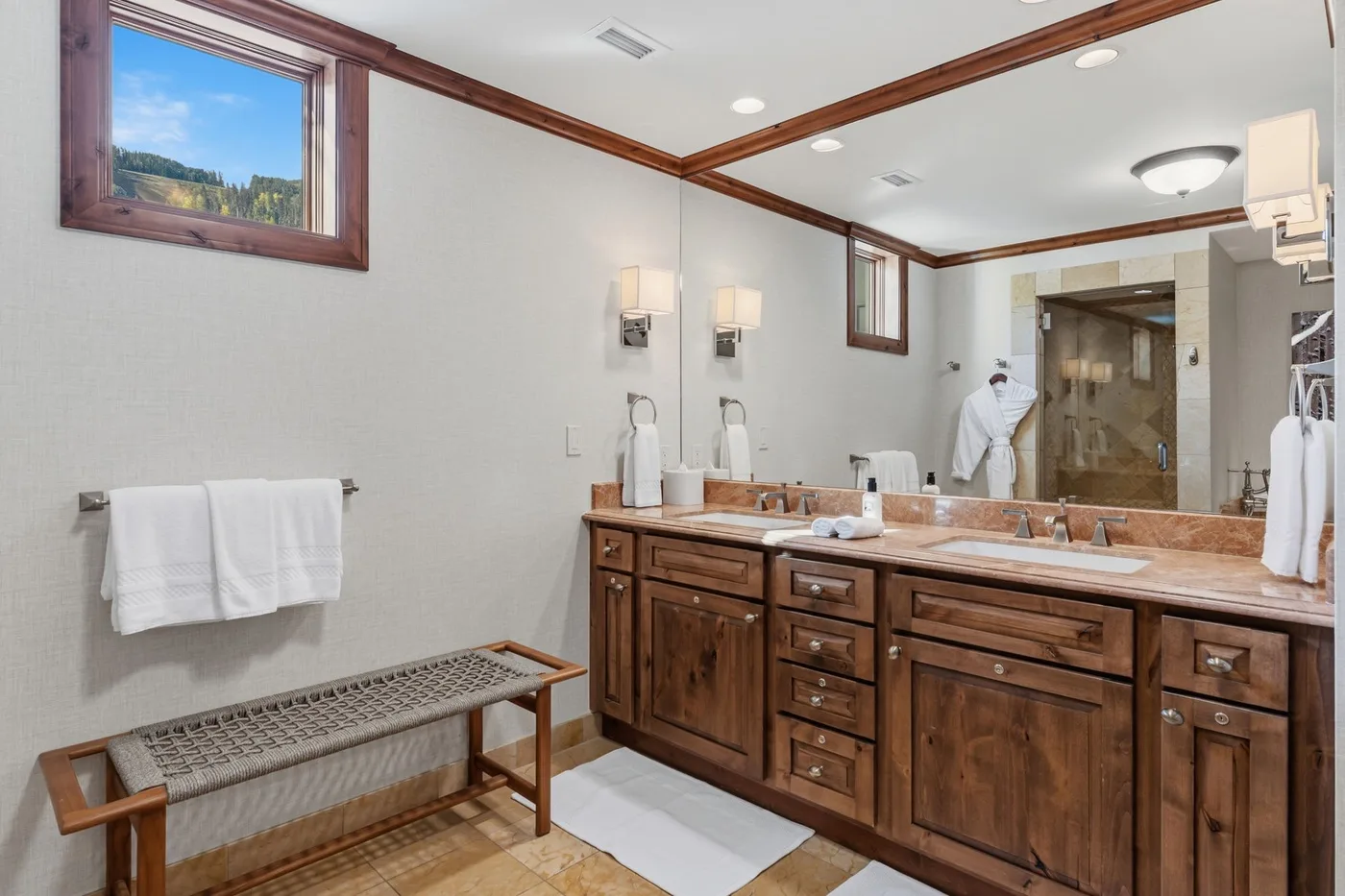 Un baño amplio con un tocador largo de madera, espejos y una ducha.