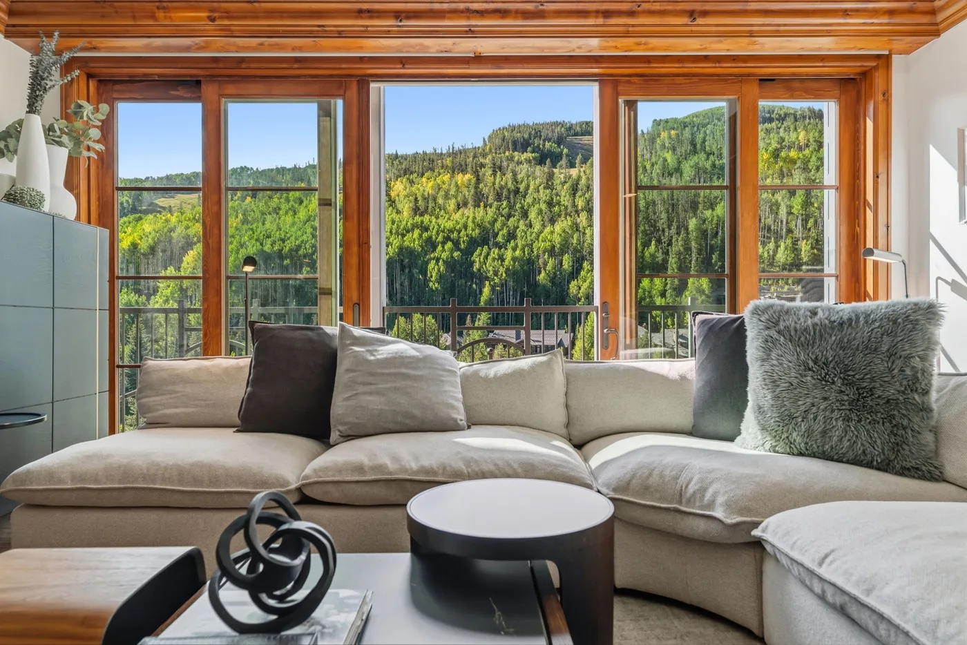 Una sala de estar con asientos seccionales y vistas a una ladera boscosa.
