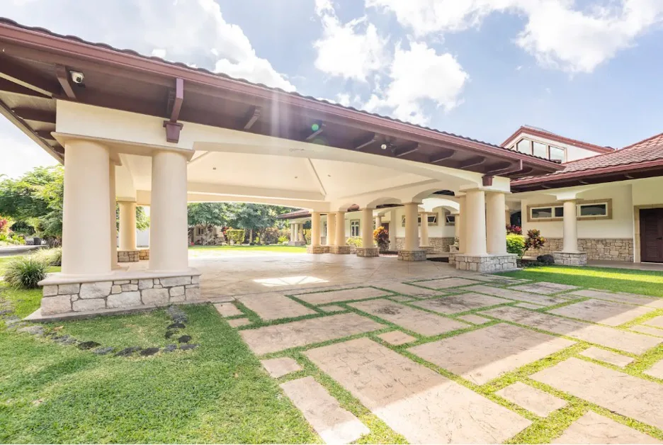 Un pasillo exterior cubierto con columnas color crema bordea un patio pavimentado.