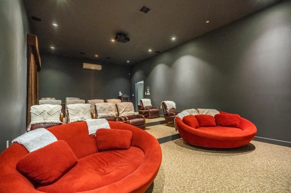 Una sala de cine oscura con asientos rojos y filas de butacas frente a la pantalla.