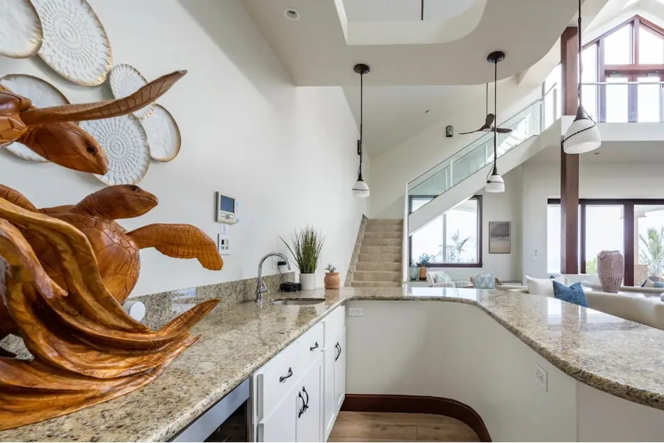 Una cocina luminosa con una encimera curva y una escalera al fondo.
