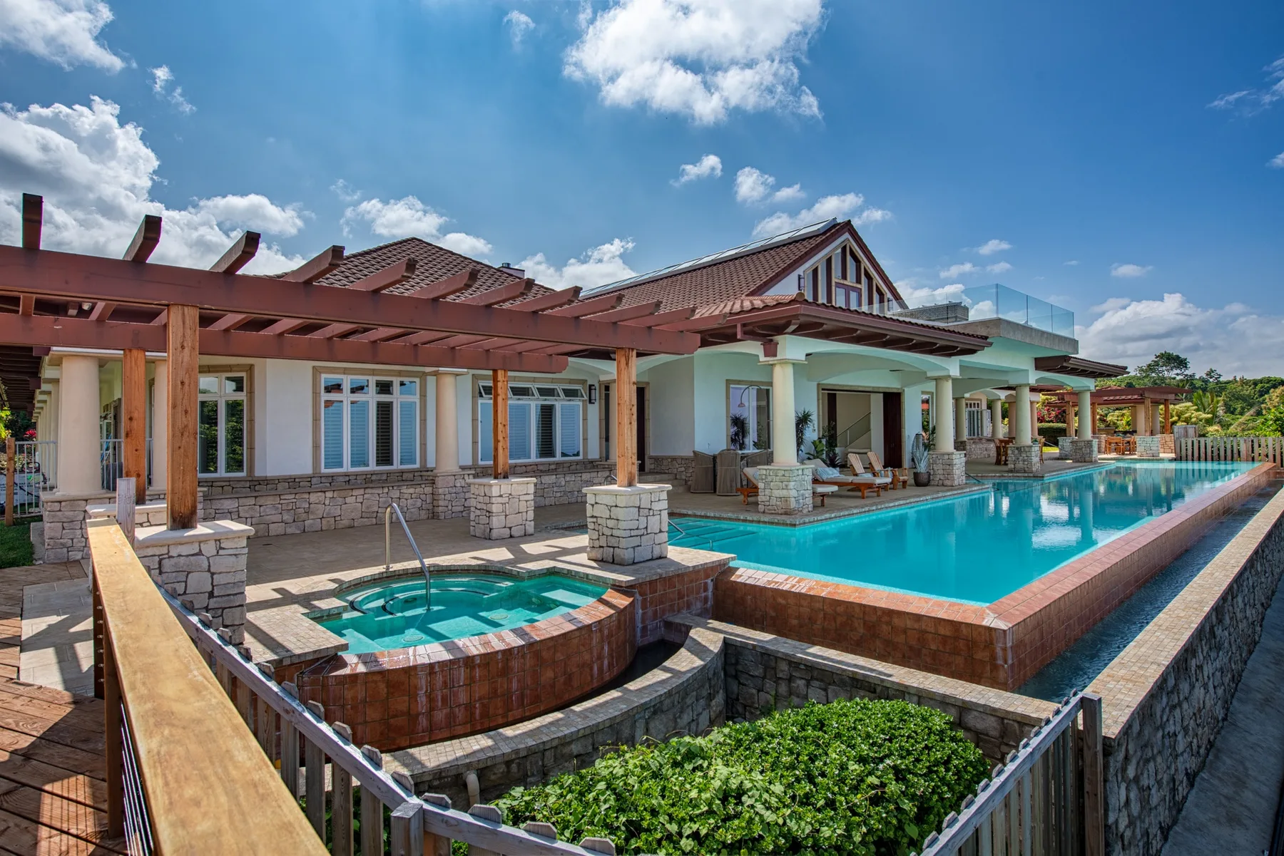 Una piscina al aire libre junto a un edificio bajo, con un pequeño jacuzzi elevado en primer plano.