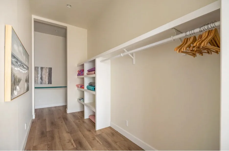 Un vestidor con estantes abiertos y perchas de madera junto a la pared.