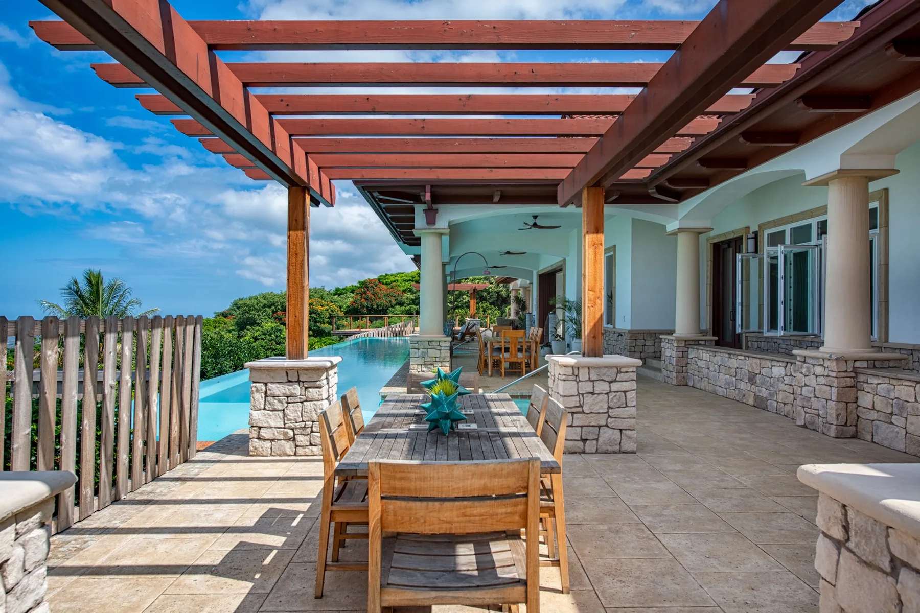 Una zona de comedor exterior cubierta junto a una piscina, con una mesa y sillas de madera.