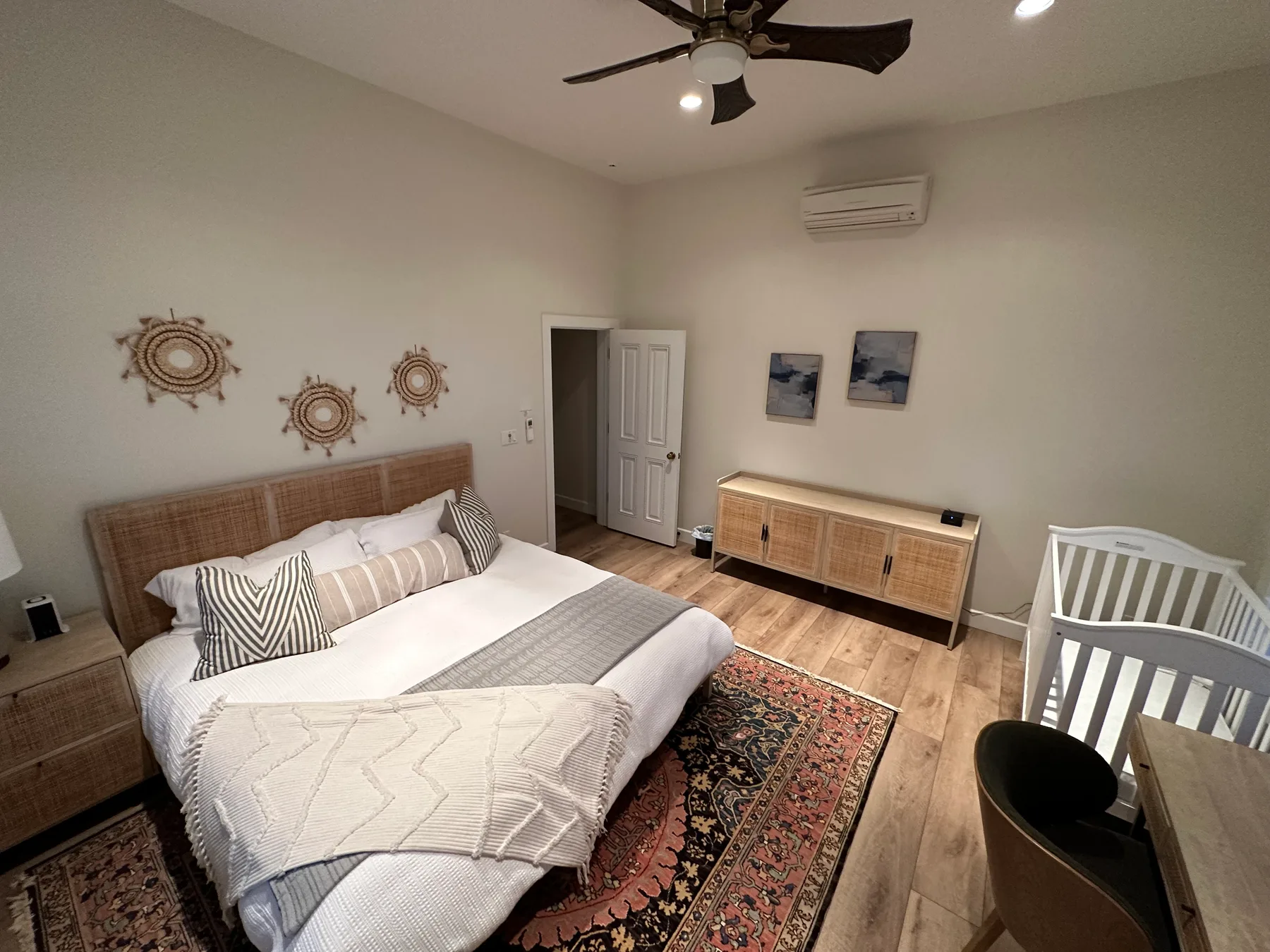 Un dormitorio con una cama, cabecero tejido y alfombras estampadas.