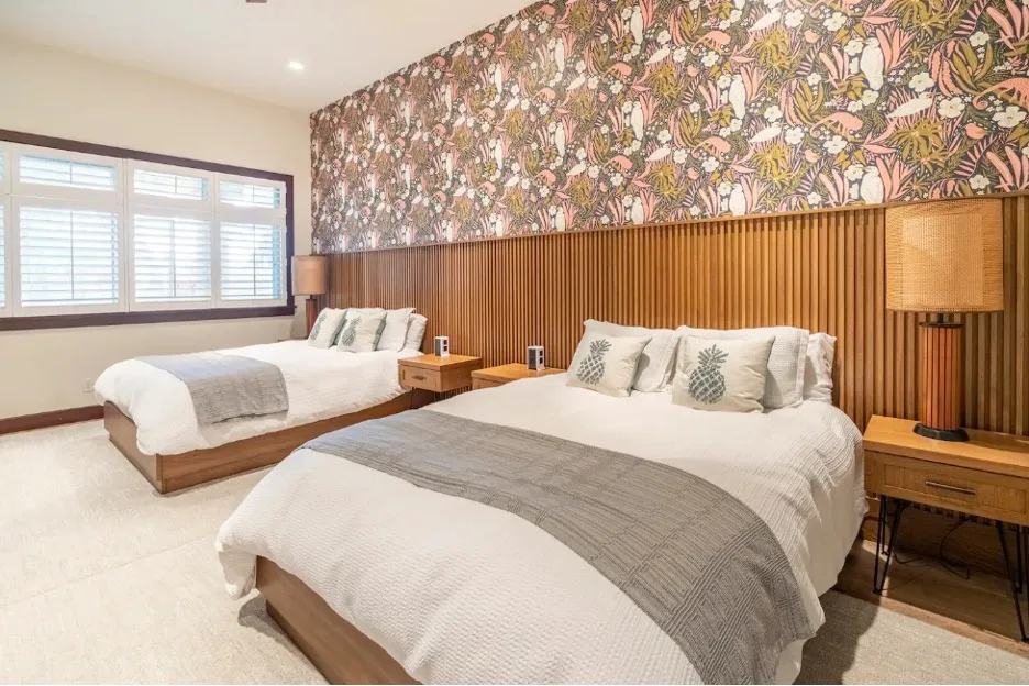 Un dormitorio con dos camas, papel tapiz estampado y una ventana con persianas.