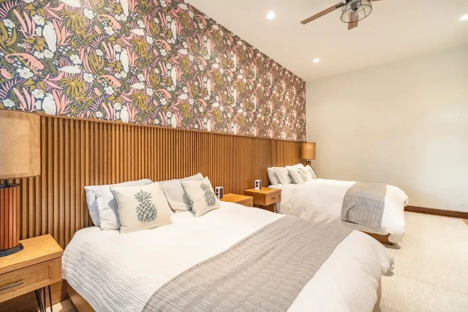 Un dormitorio con dos camas, papel tapiz estampado y paneles de madera en la pared.
