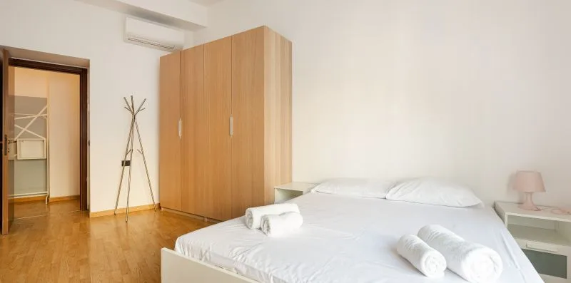 A bedroom with a bed, folded towels, and a wooden wardrobe.