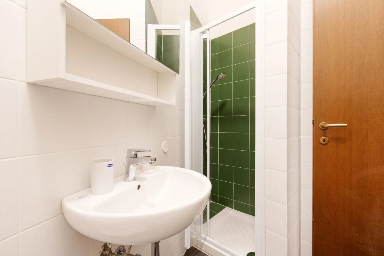 A tiled bathroom with a white sink and a green-tiled shower.
