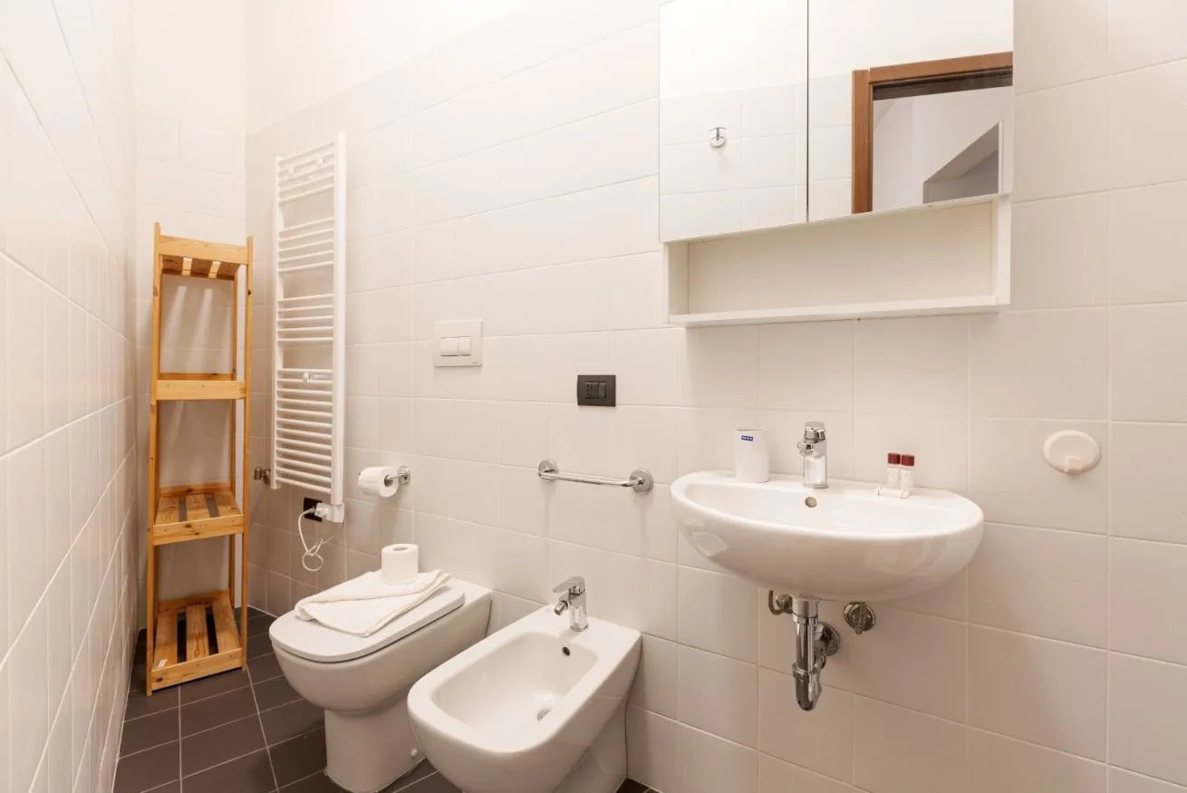 A tiled bathroom with a sink, toilet, bidet, and wall-mounted towel warmer.