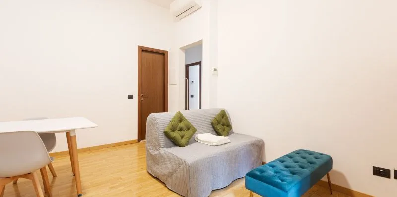 A small seating area with a gray sofa, decorative cushions, and a teal ottoman.