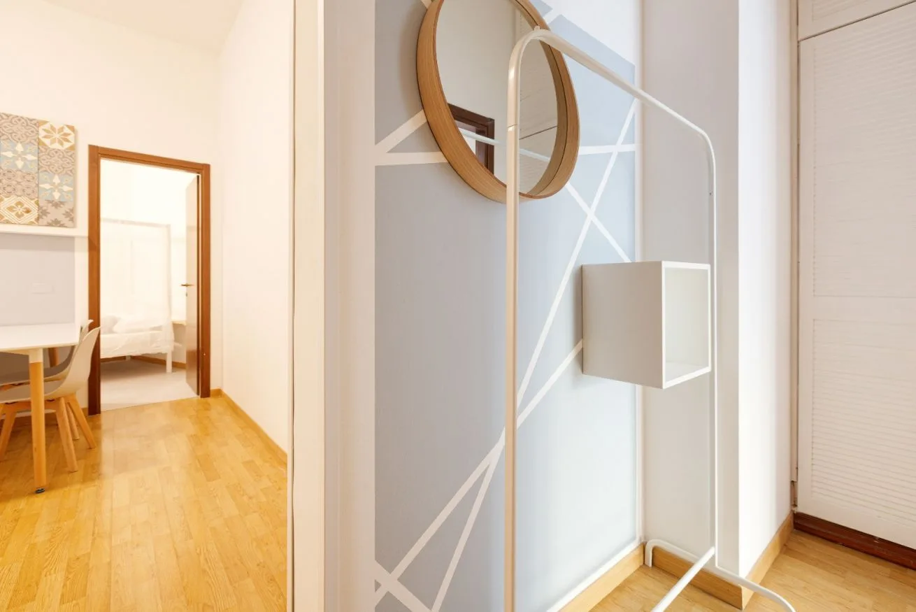 A bright interior hallway with a geometric wall design and a doorway to a furnished room.