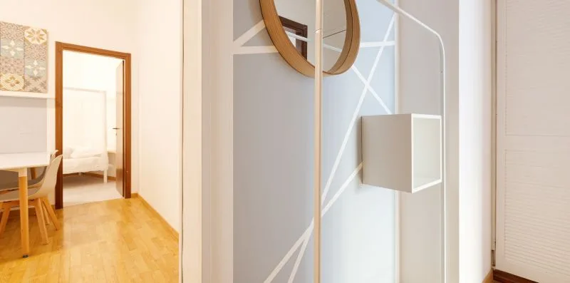 A bright interior hallway with a doorway, wall mirror, and geometric wall detailing.