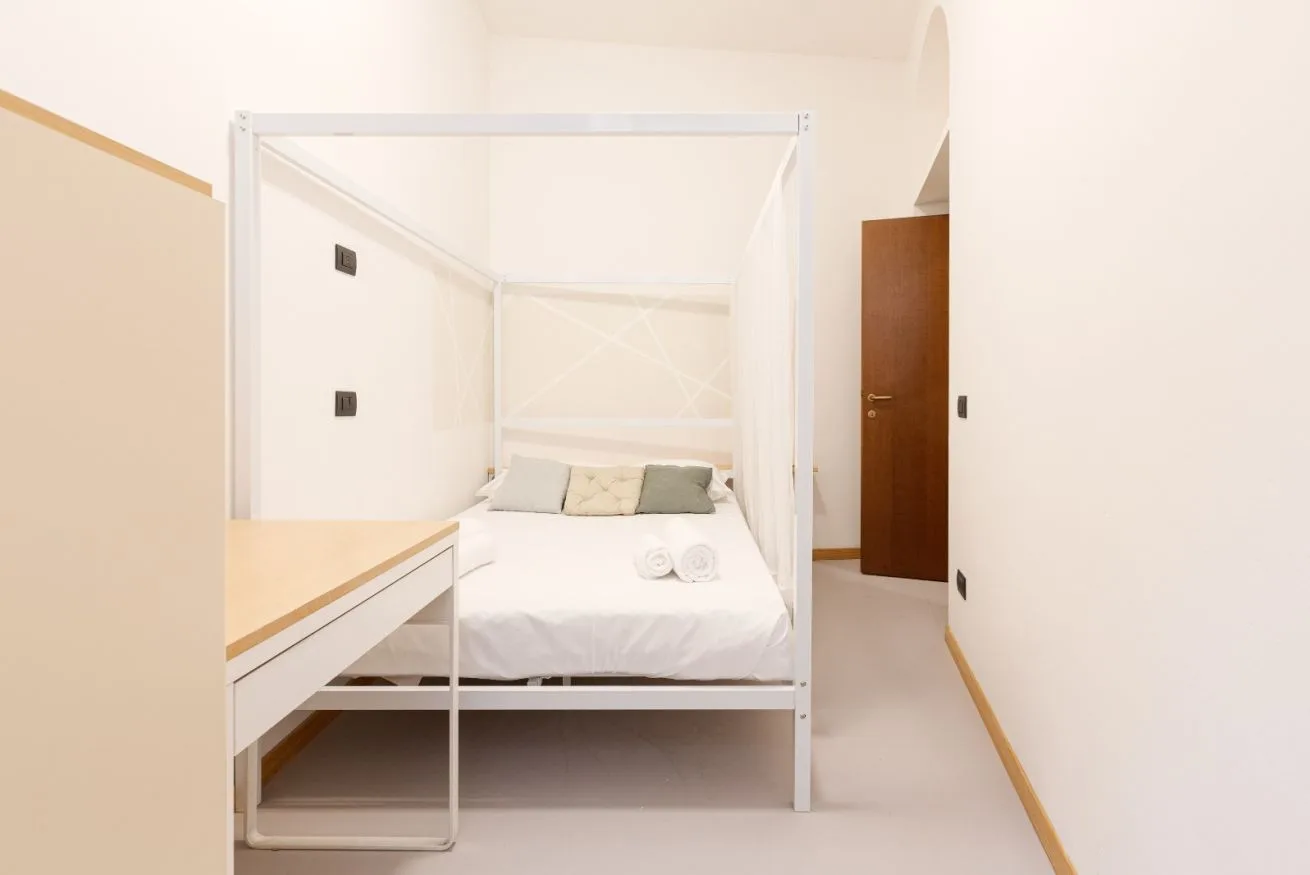 A bedroom with a white bed and a desk beside it.