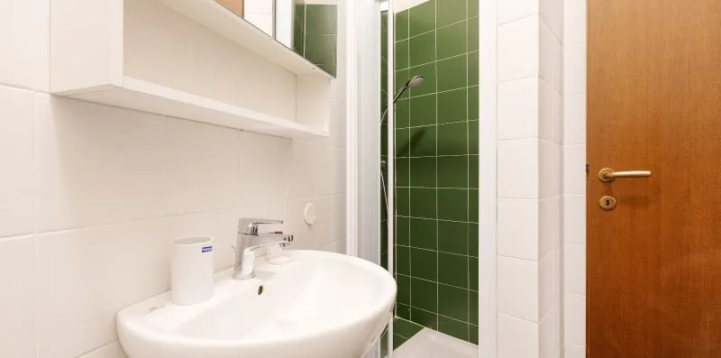 A bathroom sink sits beside a shower with green tiled walls.