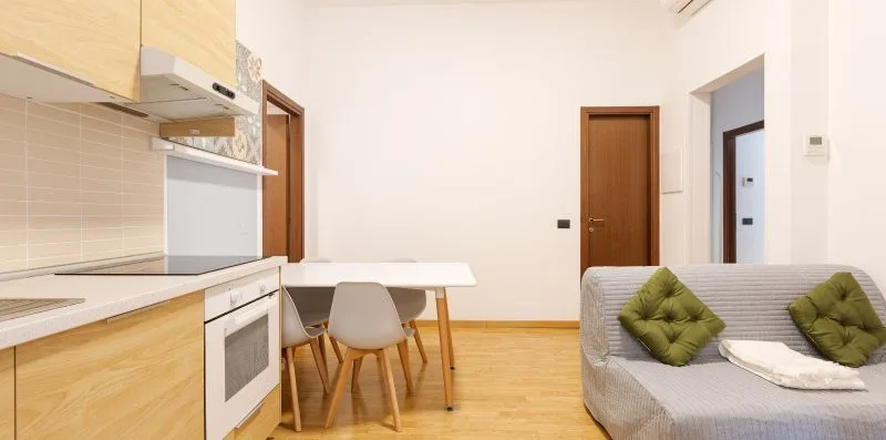 A bright kitchen and dining area opens onto a seating space with a gray sofa.