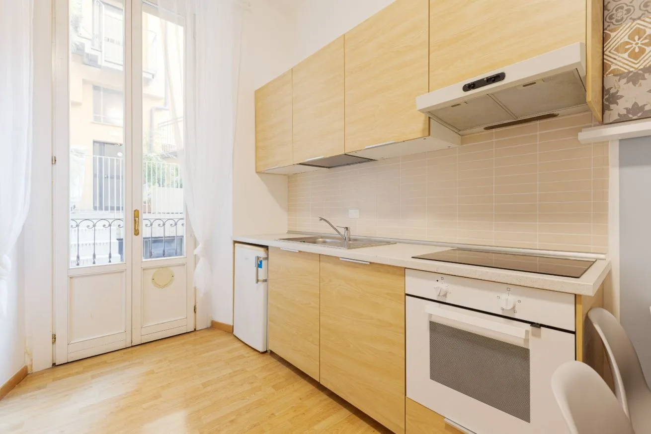 A bright kitchen with pale wood cabinets and a glass balcony door.