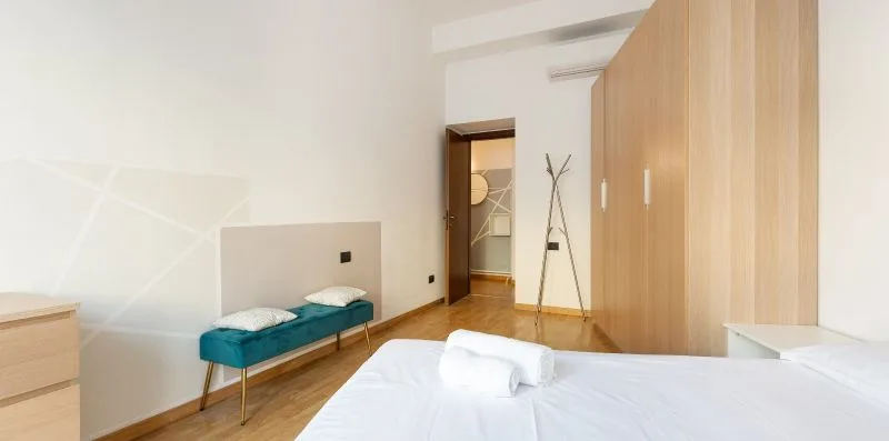 A bedroom with a bed, a teal bench, and a row of wooden wardrobes.
