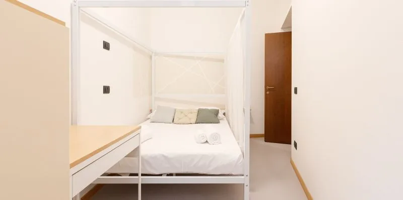 A white bed sits in a bright bedroom beside a wooden door.